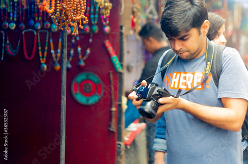 Young indian photographer shooting looking at his camera in the middle of the market in the hill town of mcleodganj in India himachal pradesh