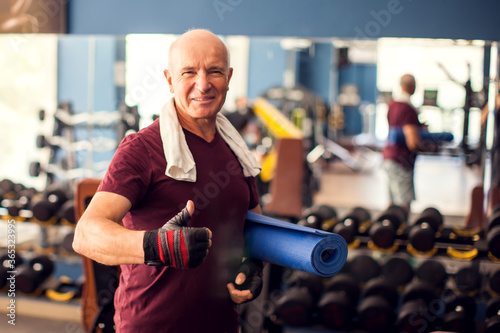 A portrait of senior man keeping yoga mat and looking at camera. People  healthcare and lifestyle concept