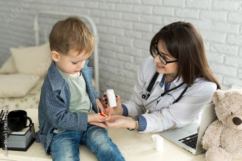 .Beautiful smiling female doctor hold in arms pill bottle and offer it to child visitor closeup.