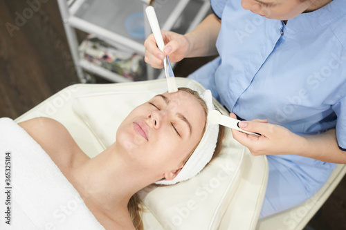 Doctor cosmetologist makes a multi-stage facial cleansing procedure to a young attractive woman in a beauty salon. Summer skin care