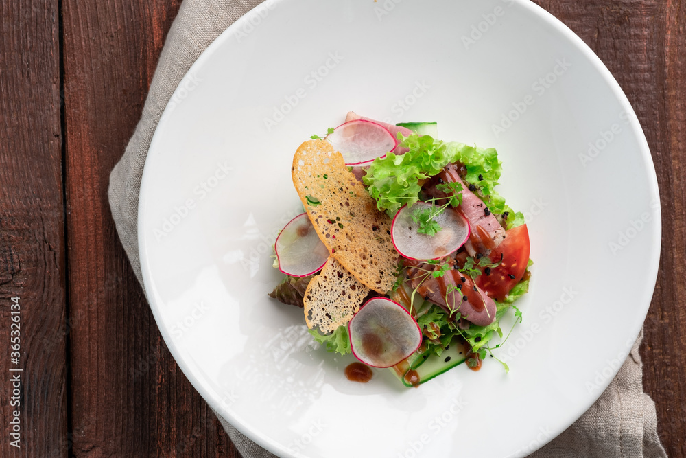 Fresh salad of greens, vegetables, radishes, cucumbers and ham in a white plate on a wooden background Fresh salad of greens, vegetables, radishes, cucumbers and ham in a white plate on a wooden background
