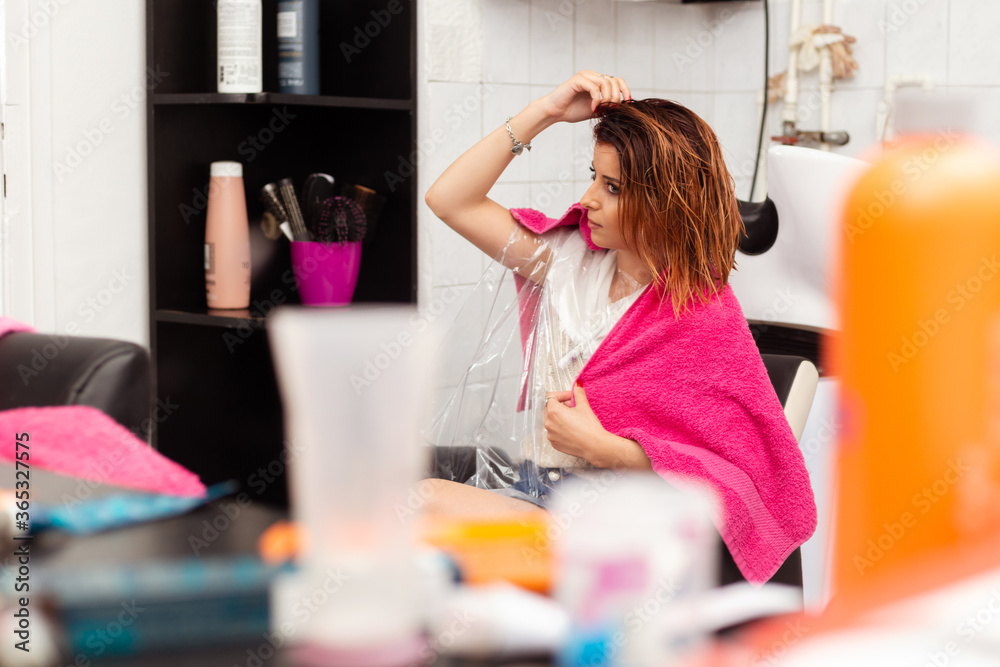 Beautiful redhead woman sitting at hairdresser salon after her hair being washed. Young female looking herself in the mirror at barber shop. Beautiful redhead woman sitting at hairdresser salon after her hair being washed. Young female looking herself in the mirror at barber shop.