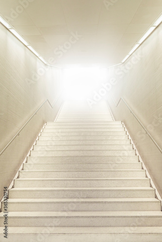 Up stairs going toward strong light. Stairs going up. White modern staircase.