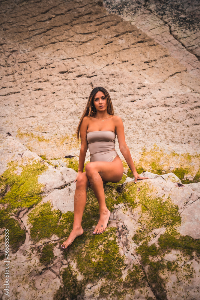 A dark-haired caucasian woman in a brown swimsuit on a natural background next to rocks and sea in the town of Zumaia, Gipuzkoa. Basque Country. In the summer sunset. Spectacular scenery A dark-haired caucasian woman in a brown swimsuit on a natural background next to rocks and sea in the town of Zumaia, Gipuzkoa. Basque Country. In the summer sunset. Spectacular scenery