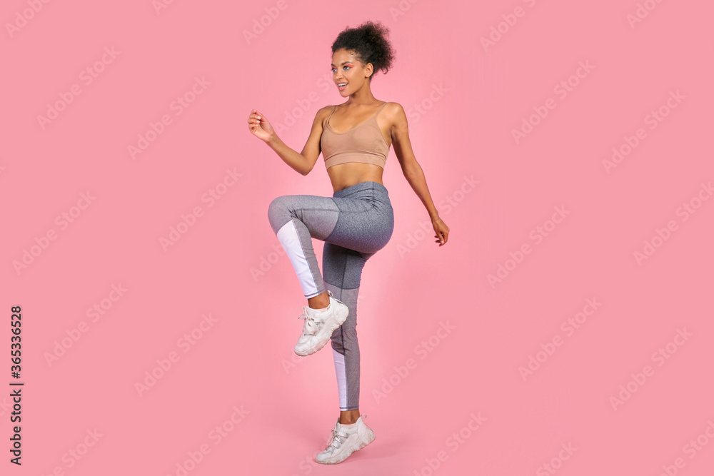 Black graceful  woman dooing fitness over pink background in studio.