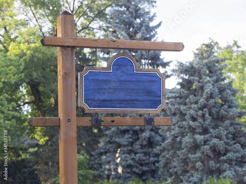 Photo of a blank empty wooden park sign post with trees in the background
