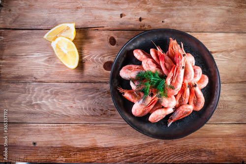 Appetizing boiled shrimp on a skewer in a black plate on a wooden surface among lemon. The concept of fast and wholesome food