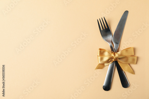 Cutlery with bow on beige background, space for text
