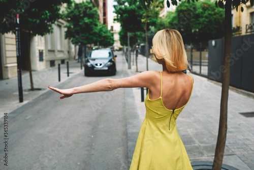Canvas Print Back view young sexy woman in yellow dress hailing a cab taxi standing on the ro