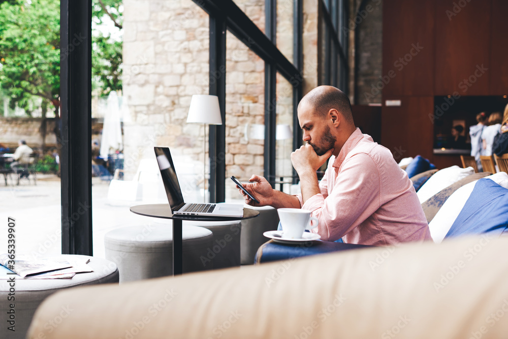 Modern business man using smart phone and laptop computer in light loft interior,young hipster busy using smart phone in hotel hall,male student reading message on phone sitting at sofa of coffee shop Modern business man using smart phone and laptop computer in light loft interior,young hipster busy using smart phone in hotel hall,male student reading message on phone sitting at sofa of coffee shop
