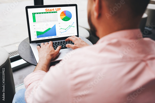 Experienced businessman looking at financial data with graphics and charts while work on a laptop computer, young entrepreneur typing text on notebook keyboard, male freelancer analyzing performance