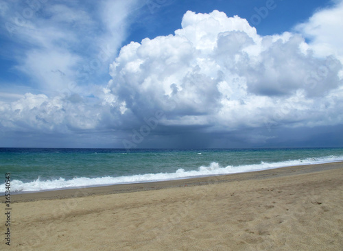 Sandy beach on a warm summer day, turquoise sea with glebe waves and large rain clouds over the sea, Italy, Calabria