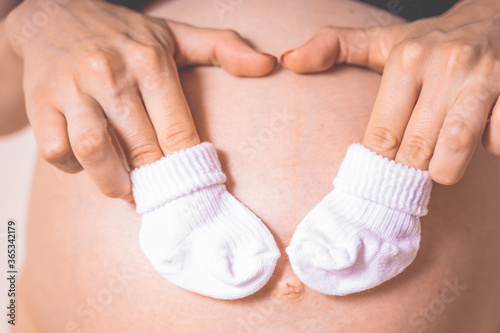 Pregnant woman with clothing for newborn baby close up. White woolen little baby slippers, socks in future mom hands..Symbol of happy pregnancy.