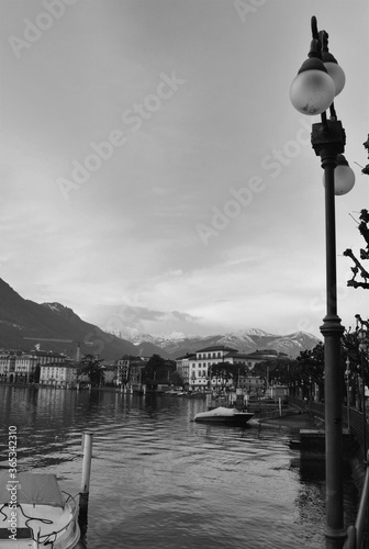Black and white artistic photo of a Swiss landscape in winter. Water, vintage lantern and silhouettes of alps in the fog in the background © Vadim