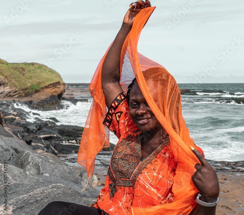 African woman with orange dress on the cliffs by the sea in Sekondi-Takoradi Ghana West Africa photo