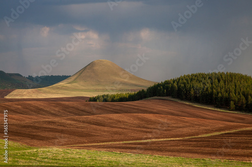 A hilly area with a plowed field and solitary mountains and a gloomy sky.