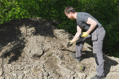 A man working with a shovel near a heap of soil.