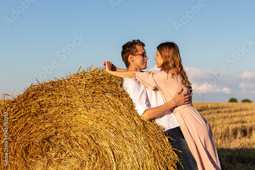 Portrait of couple in love in field in countryside. A young woman in pink dress hugging her boyfriend.