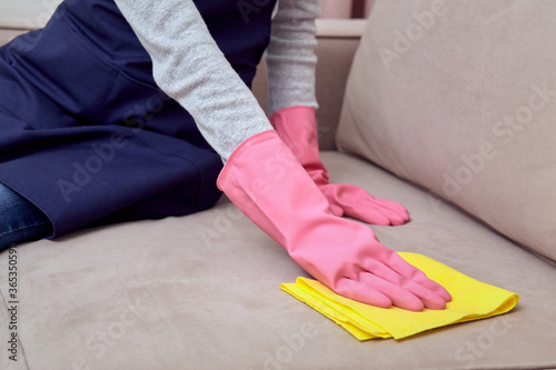 A beautiful young girl in a pink glove washes the sofa with a rag for cleaning.