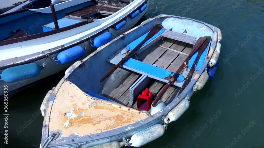 A weathered old dinghy rowing boat rocking about tied up to a pontoon in a marina. A weathered old dinghy rowing boat rocking about tied up to a pontoon in a marina.