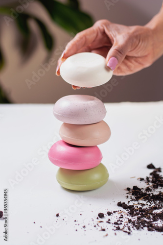 mano de mujer colocando  jabones naturales en barra de color verde crema blanco morado y rojo en una mesa r  stica  formando una pila