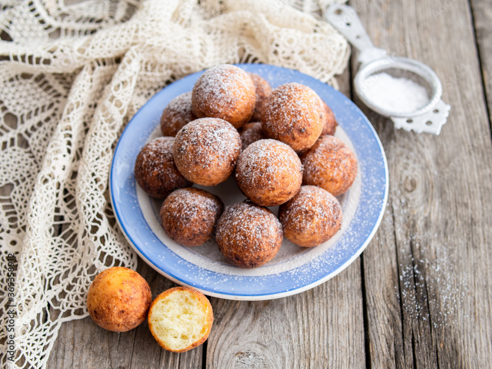 Freshly baked cheese donuts with powdered sugar on the plate on wooden rustic table. The atmosphere of a cozy home breakfast. Close up, copy space.