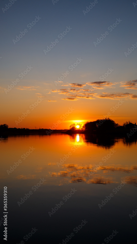 Sunset on the lake, the sun sets behind the trees and beautiful reflections in the water