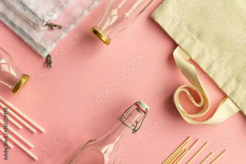Fabric cotton shopping bags, glass bottles, paper straws and wooden sticks on a pink background. Top view. Copy space.