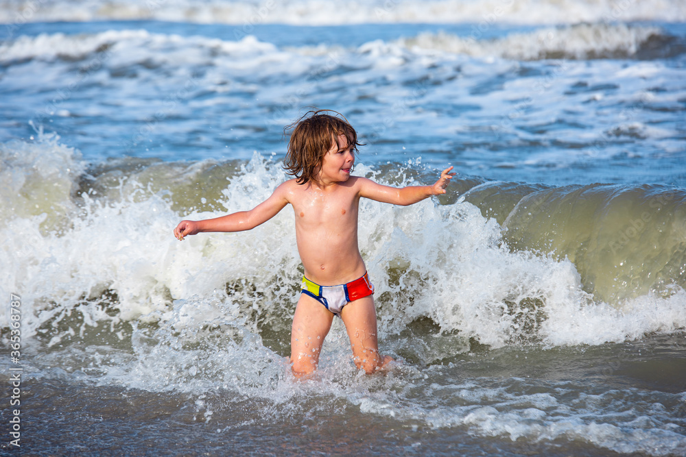 Little boy playing in outdoor jumping into water on summer vacation on tropical beach island. Happy child playing in the sea.