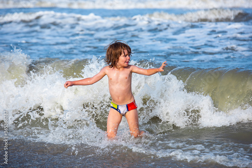 Little boy playing in outdoor jumping into water on summer vacation on tropical beach island. Happy child playing in the sea.