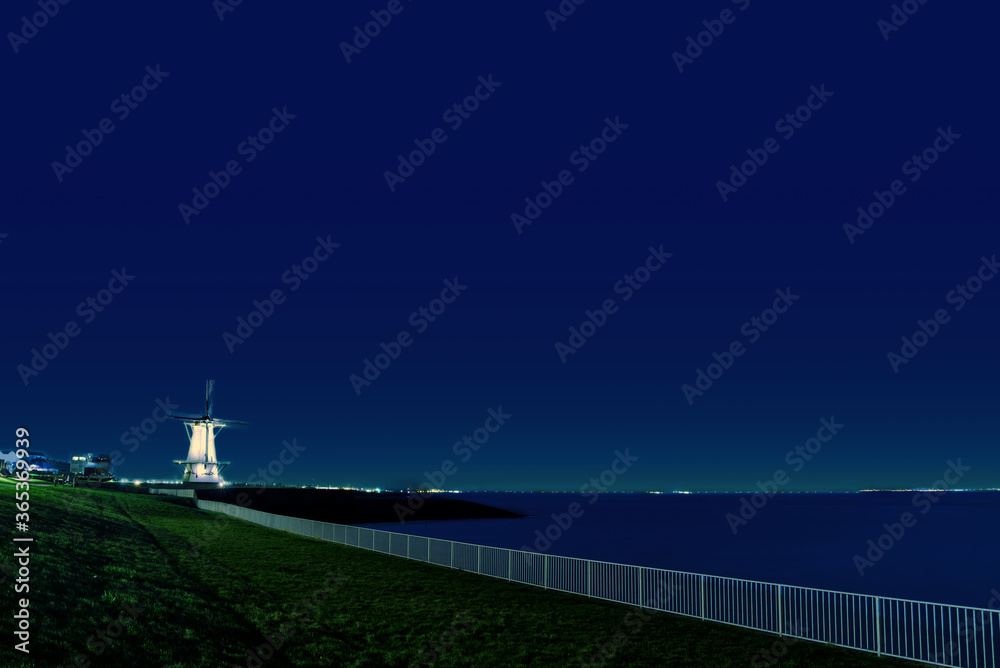 Seaside railings and windmill under dark blue sky, tranquil night, Vlissingen in Netherlands