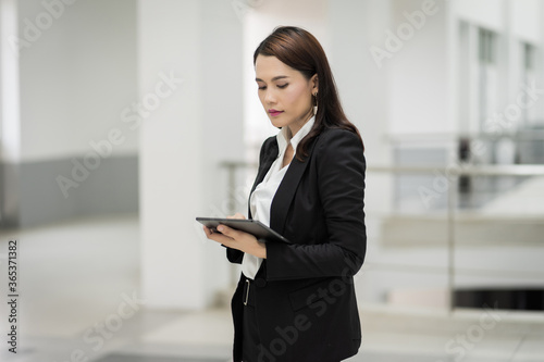 Portrait of a young cheerful businesswoman surfing social network on digital tablet in front of office during break. Asian business woman standing in office building. Business stock photo