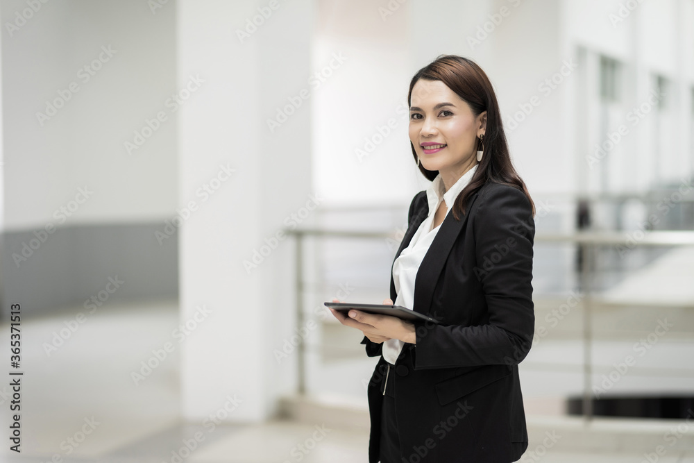 Portrait of a young cheerful businesswoman surfing social network on digital tablet in front of office during break. Asian business woman standing in office building. Business stock photo Portrait of a young cheerful businesswoman surfing social network on digital tablet in front of office during break. Asian business woman standing in office building. Business stock photo