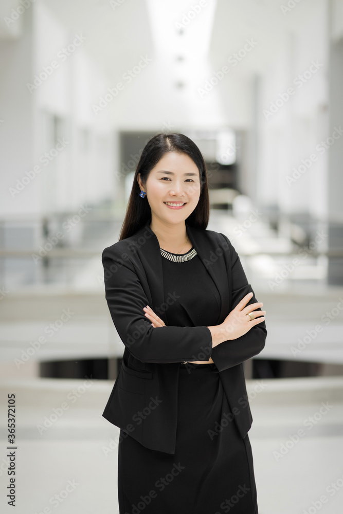 Portrait of a cheerful middle-age businesswoman in business suit stands in the company building with confidence arms crossed. Modern business woman in the office with copy space. Business stock photo.