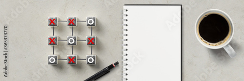 cube grid with tic tac toe game besides notepad and coffee on concrete background