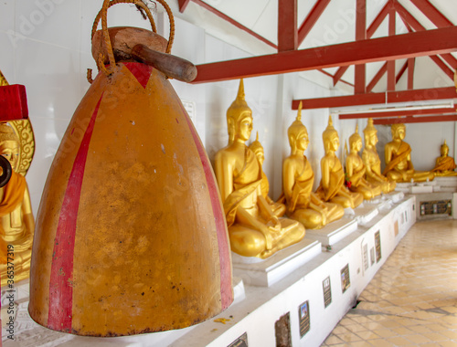 The hammer lies on a traditional bell in the Buddhist Monastery, on the background of the gilded statue of Buddha, Photharam, Thailand. photo