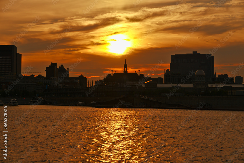 A skyline of Montreal Old Port at sunset. Foreground is Saint Laurent river.
