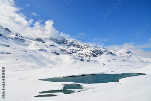 View of snow mountain and small partial frozen lake along Bernina Express train near Ospizio Bernina