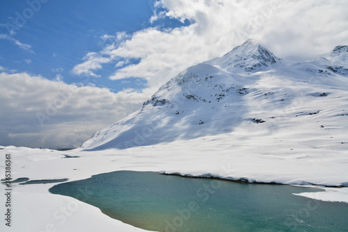 View of snow mountain and small partial frozen lake along Bernina Express train near Ospizio Bernina