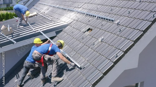 Wallpaper Mural Three Caucasian young men standing on steep residential rooftop installing solar panel metal hardware strip with electric portable hand drill, aerial profile close up Torontodigital.ca