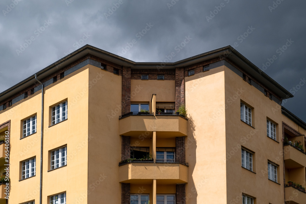 Deunkle Gewitterwolken über einem von der Sonne beschienenem Wohnhaus an der Wisbyer Strasse in Berlin