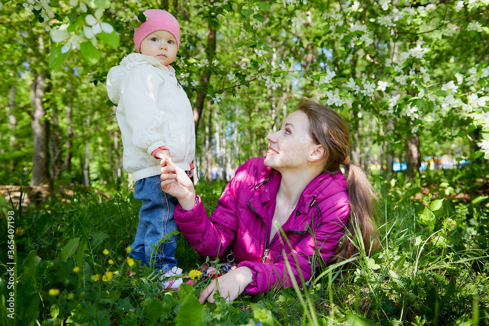Portrait of young mother and her small daughter in the park full of apple blossom trees in a spring day. Woman and girl in nature landscape