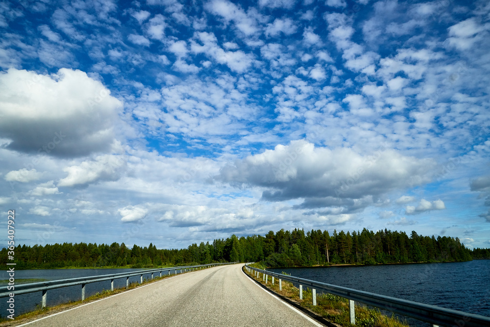 Beautiful landscape with blue sky, white clouds, water of lake and the road that goes to the horizon.