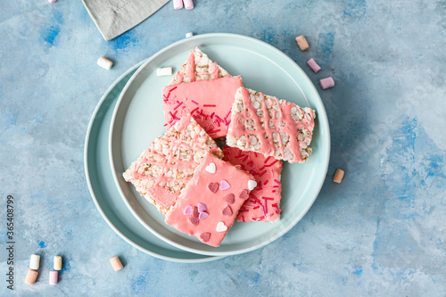 Plates with crispy rice bars and marshmallow on color background photo