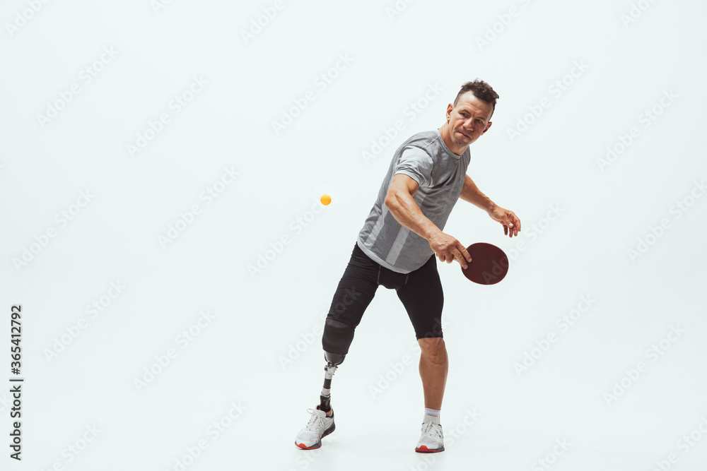 Athlete with disabilities or amputee isolated on white studio background. Professional male table tennis player with leg prosthesis training in studio. Disabled sport and healthy lifestyle concept. Athlete with disabilities or amputee isolated on white studio background. Professional male table tennis player with leg prosthesis training in studio. Disabled sport and healthy lifestyle concept.