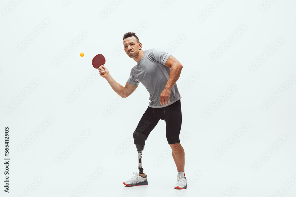 Athlete with disabilities or amputee isolated on white studio background. Professional male table tennis player with leg prosthesis training in studio. Disabled sport and healthy lifestyle concept. Athlete with disabilities or amputee isolated on white studio background. Professional male table tennis player with leg prosthesis training in studio. Disabled sport and healthy lifestyle concept.