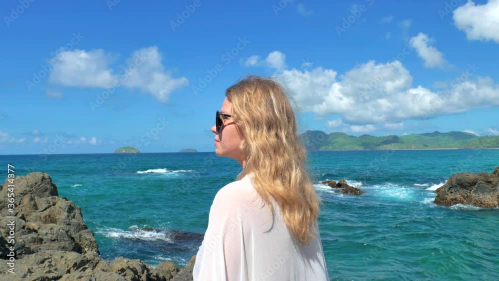 Back view of young girl standing near waves hitting the rocks Young girl looking out to ocean,, waves breaking against the stones. Travel concept. Palawan, Philippines. Back view of young girl standing near waves hitting the rocks Young girl looking out to ocean,, waves breaking against the stones. Travel concept. Palawan, Philippines.