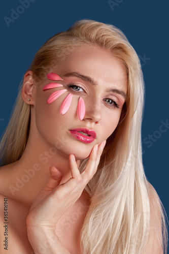 Beauty face. Ayurveda treatment. Blonde woman with flower petals creative makeup isolated on blue.