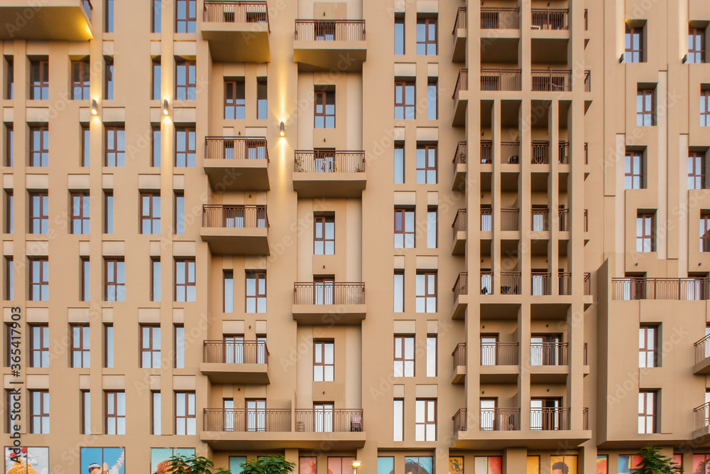 Sand color facade of modern residenial building, with rows of small windows and balconies, front view.