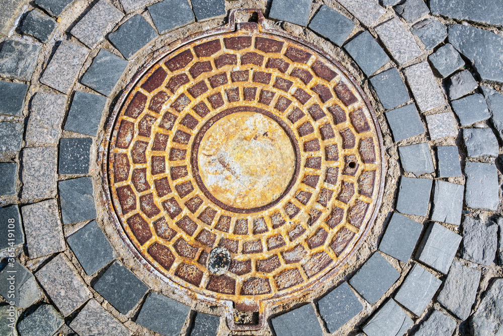 Close up of old sewer manhole cover on the urban road.
